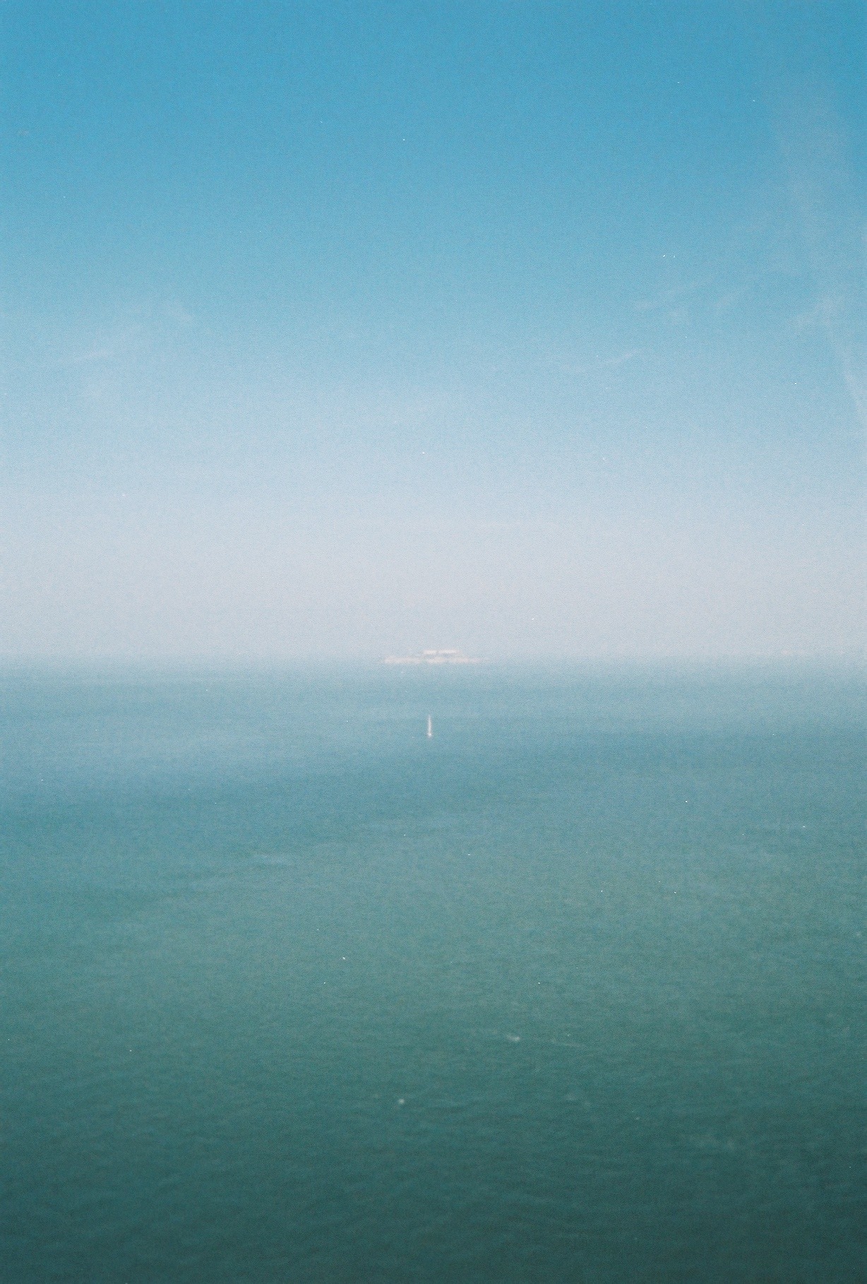 sailboat floats in front of hazy Alcatraz