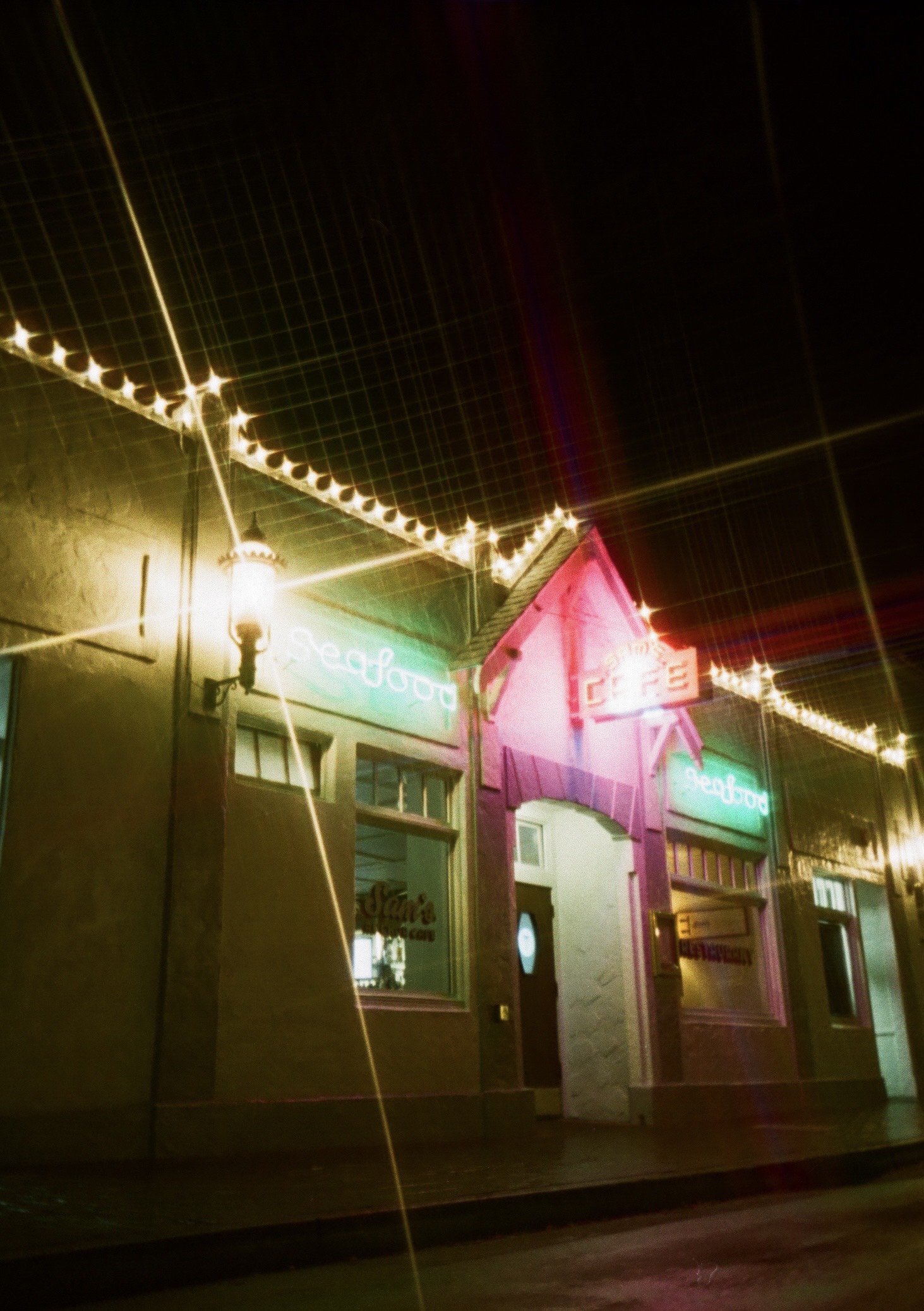 neon lights from a cafe reflect off wet pavement